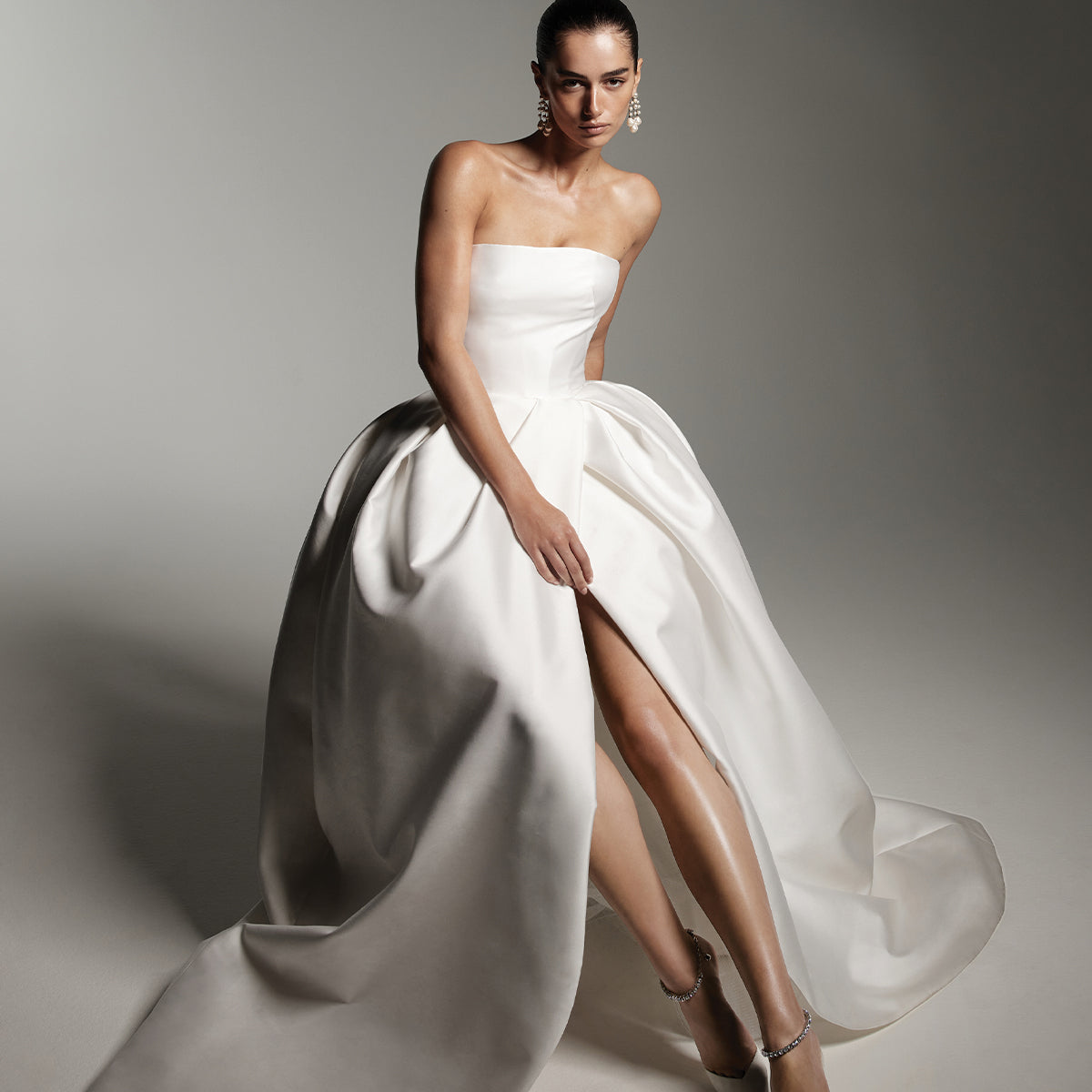 Model wearing Monique Lhuillier Spring 2026 Bridal white mikado Doheny strapless corset bodice tulip skirt ball gown with front skirt slit