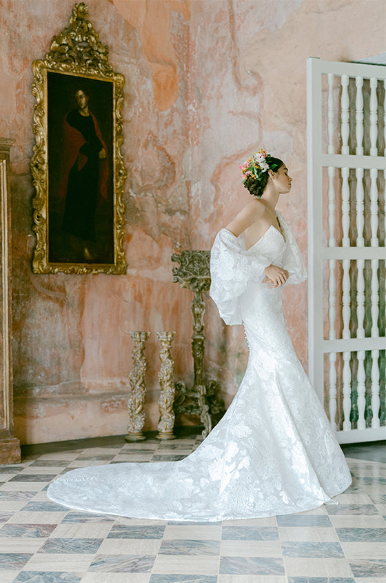Woman wearing Monique Lhuillier Fall 2022 white fitted floral organza Delilah gown with billowing Delilah jacket