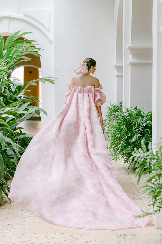 Woman wearing Monique Lhuillier Fall 2022 pink floral Petal cocktail dress with puff sleeve and long matching Petal cape