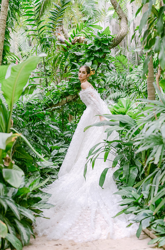 Woman wearing Monique Lhuillier Fall 2022 white daisy appliqued Regency ballgown with matching Regency cape