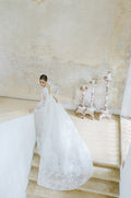 Woman wearing Monique Lhuillier Fall 2022 white embroidered lace Royalty ballgown with matching Royalty long sleeve jacket