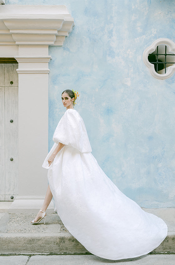 Woman wearing Monique Lhuillier Fall 2022 high-low jacquard Adele ballgown with matching Adele billowing jacket