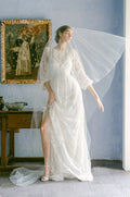 Woman wearing Monique Lhuillier Fall 2022 long sleeve white beaded sheath Emma gown with sheer veil over face