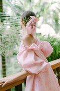 Woman wearing Monique Lhuillier Fall 2022 pink floral Petal cocktail dress with puff sleeve and long matching Petal cape