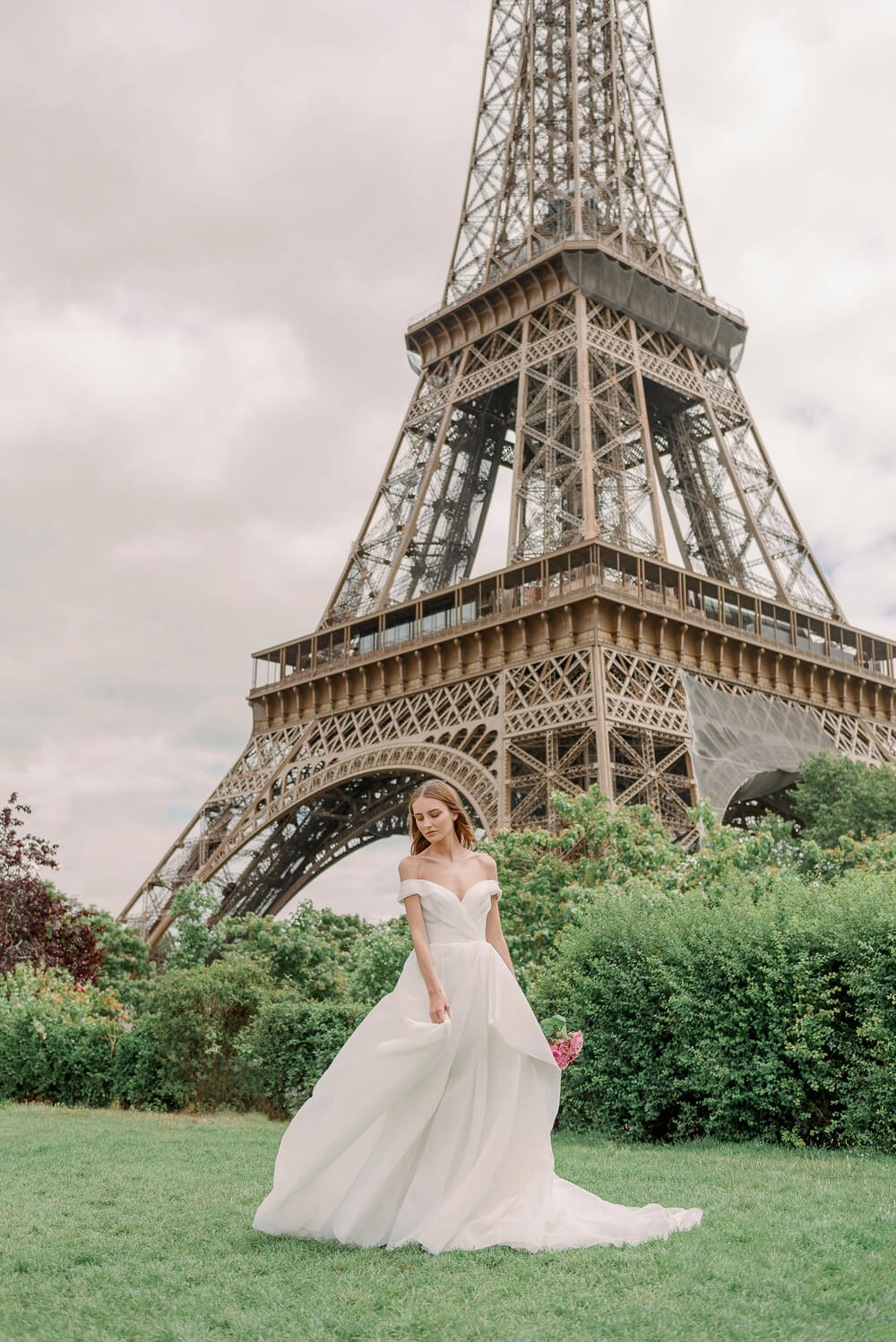 Woman wearing Monique Lhuillier Spring 2024 Bliss white organza off-the-shoulder draped bodice BL24102 ballgown