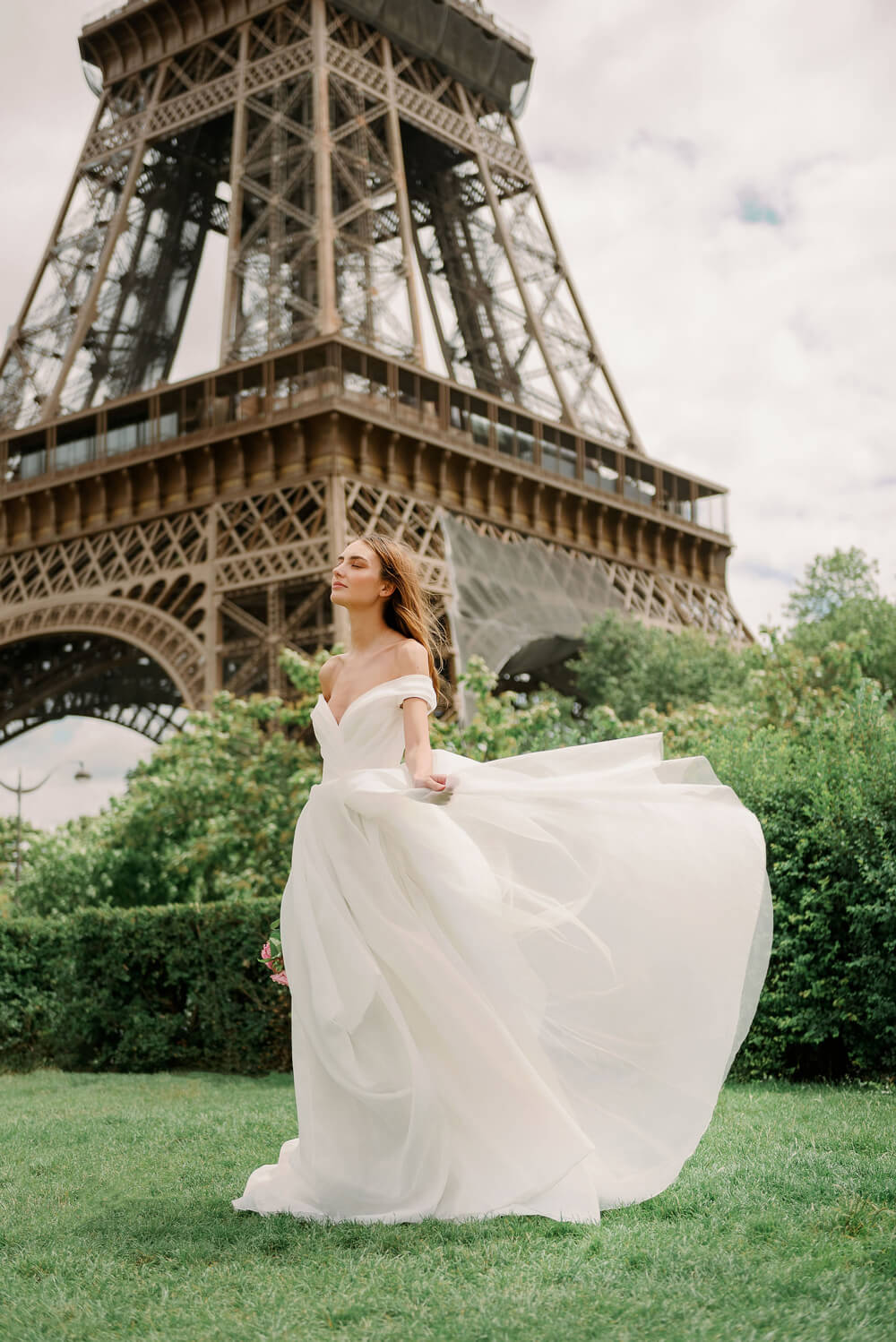 Woman wearing Monique Lhuillier Spring 2024 Bliss white organza off-the-shoulder draped bodice BL24102 ballgown
