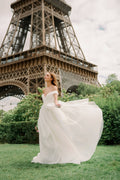 Woman wearing Monique Lhuillier Spring 2024 Bliss white organza off-the-shoulder draped bodice BL24102 ballgown