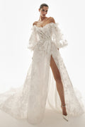 Model wearing Monique Lhuillier Spring 2026 Bridal white Topanga embroidered threadwork organza strapless draped bodice ethereal gown with detachable billowed sleeves and skirt slit