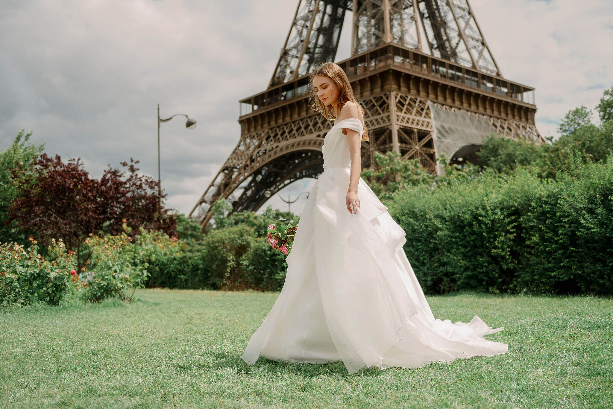 Woman wearing Monique Lhuillier Spring 2024 Bliss white organza off-the-shoulder draped bodice BL24102 ballgown