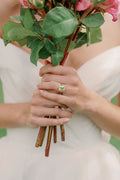 Woman wearing a peridot and diamond engagement ring wearing Monique Lhuillier Spring 2024 Bliss white organza draped bodice BL24102 ballgown
