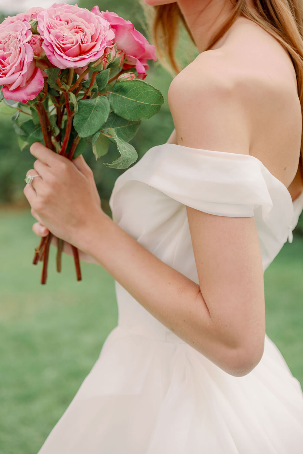 Woman wearing a peridot and diamond engagement ring wearing Monique Lhuillier Spring 2024 Bliss white organza draped bodice BL24102 ballgown