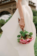 Woman holding a bouquet of flowers wearing Monique Lhuillier Spring 2024 Bliss white organza draped bodice BL24102 ballgown