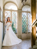 Woman wearing Monique Lhuillier Fall 2024 white mikado strapless fitted Sloane trumpet gown with detachable lace opera-length sleeves