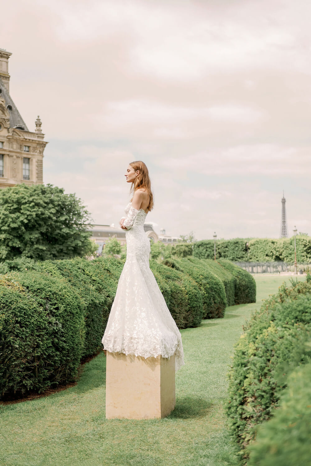 Woman wearing Monique Lhuillier Spring 2024 Bliss white embroidered lace BL24013 trumpet gown with detachable off-the-shoulder lace sleeves