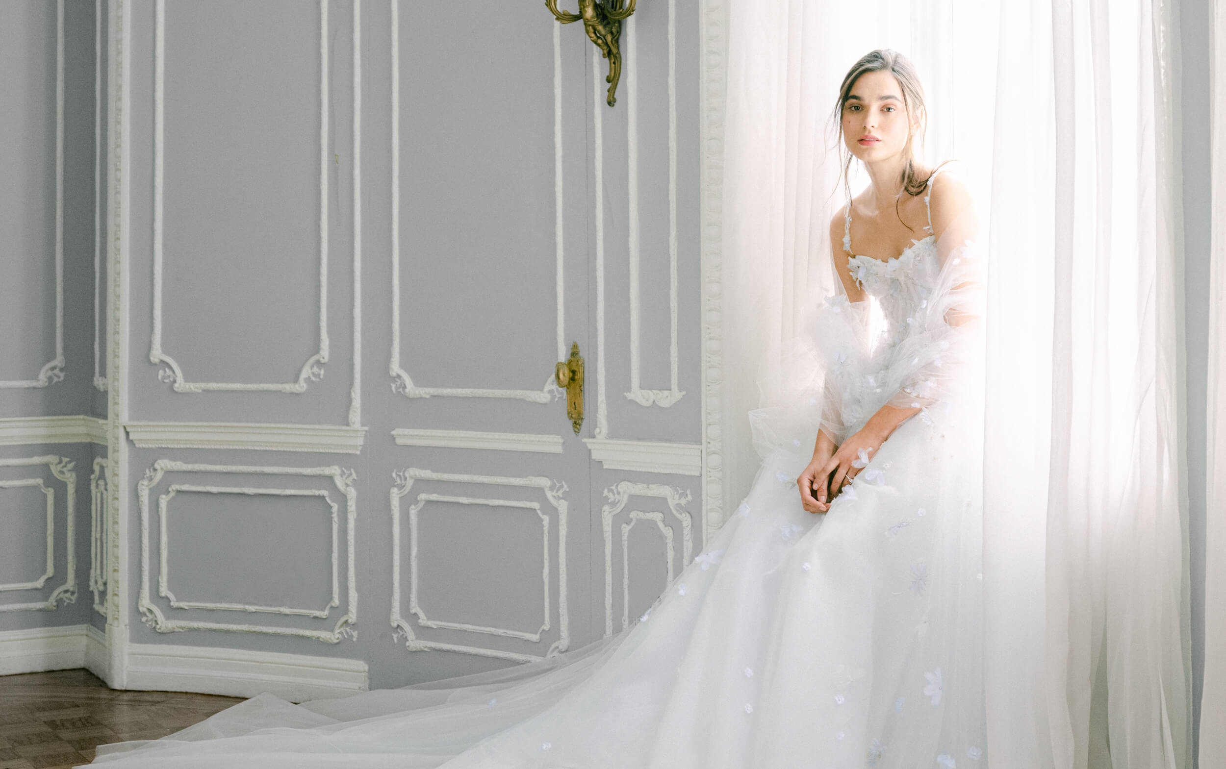 Woman sitting in window wearing Monique Lhuillier Fall 2021 sweetheart spaghetti strap pale blue Dove ballgown with 3-D applique 