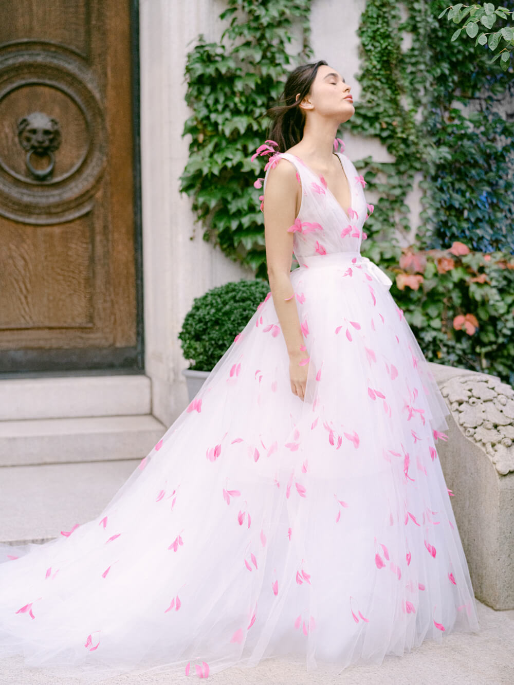 Woman wearing white Monique Lhuillier Fall 2021 tulle v-neck a-line gown with bright pink feather applique