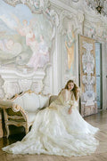 Woman sitting in yellow and green floral print Monique Lhuillier Spring 2022 Buttercup a-line gown with billow sleeves and long train