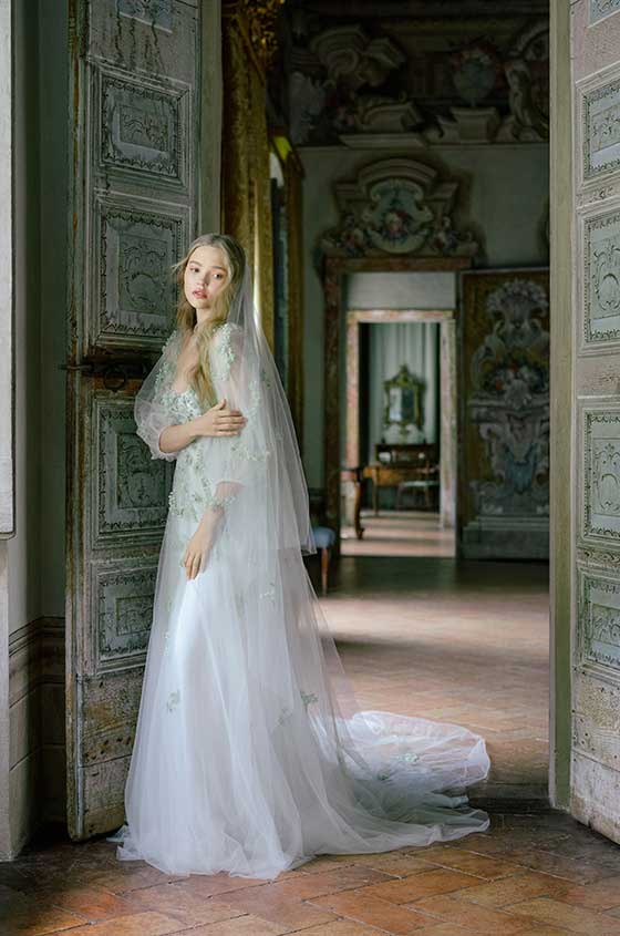Woman wearing Spring 2022 Monique Lhuillier white 3/4 sleeve Wildflower sheath gown with green 3D floral embroidery