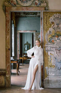 Woman wearing Monique Lhuillier Spring 2022 white crepe high neck Como sheath gown with billowed sleeve and slit