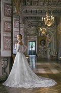 Woman wearing Monique Lhuillier Spring 2022 Fleur de Lis white lace a-line gown with matching off-the-shoulder long sleeve lace jacket