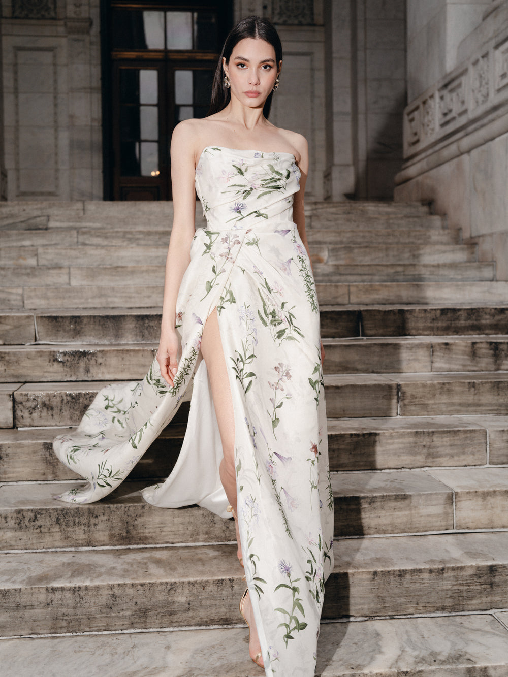 Monique Lhuillier Fall 2025 strapless, floor length gown with draped bodice and high leg slit in ivory floral multi printed gazar fabric on lookbook model.