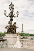 Woman wearing Monique Lhuillier Spring 2024 Bliss white embroidered lace and mikado BL24014 trumpet gown with lace long sleeve jacket