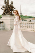 Woman wearing Monique Lhuillier Spring 2024 Bliss white embroidered lace and mikado BL24014 trumpet gown with lace long sleeve jacket