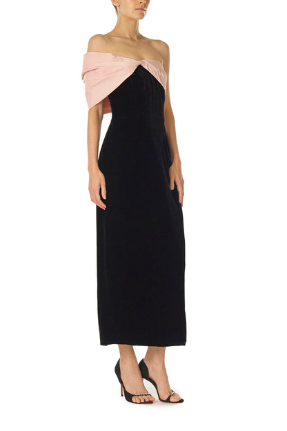 Monique Lhuillier Fall 2024 black velvet off the shoulder sheath dress with pale blush draped, asymmetric twist detail at neckline - right side.