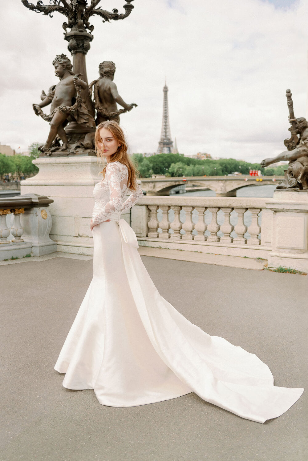 Woman wearing Monique Lhuillier Spring 2024 Bliss white embroidered lace and mikado BL24014 trumpet gown with lace long sleeve jacket