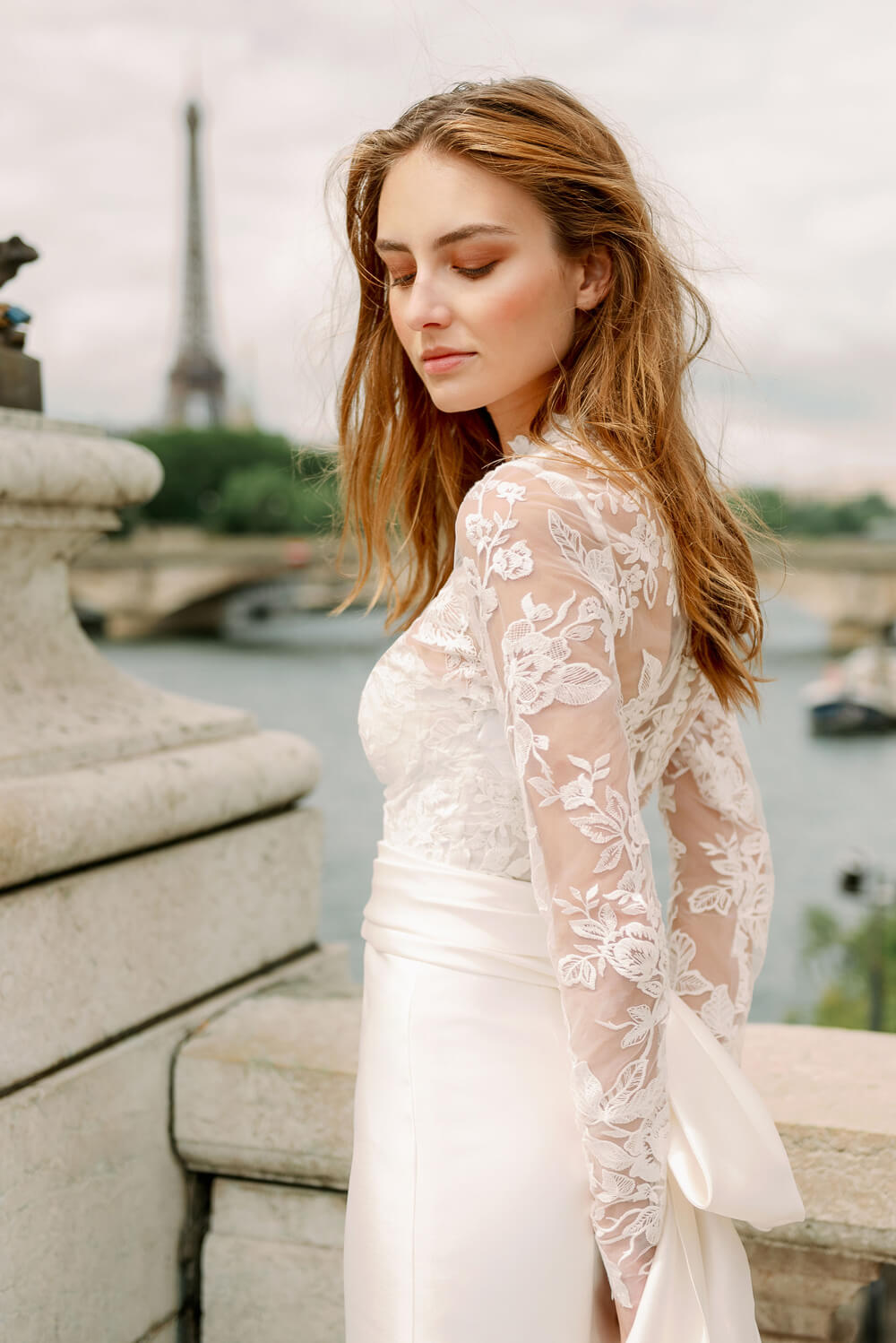 Woman wearing Monique Lhuillier Spring 2024 Bliss white embroidered lace and mikado BL24014 trumpet gown with lace long sleeve jacket