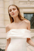 Woman wearing Monique Lhuillier Fall 2023 Bliss white off-the-shoulder crepe and mikado fitted BL23204 gown with detachable bow train