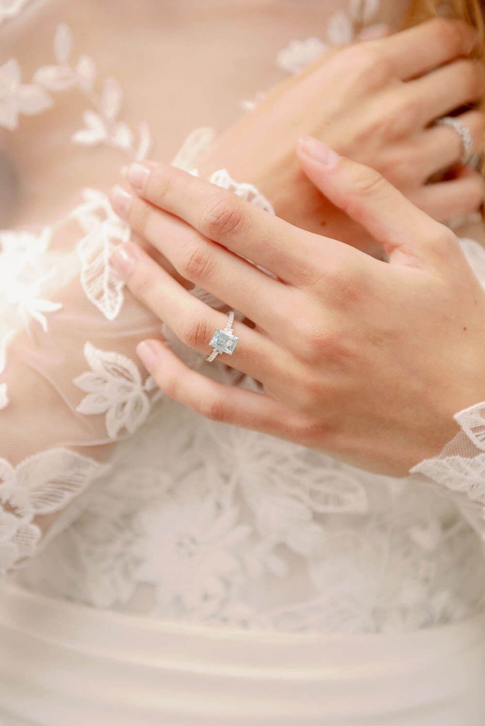 Woman wearing aquamarine and diamond engagement ring in Monique Lhuillier Spring 2024 Bliss white lace and mikado BL24014 trumpet gown