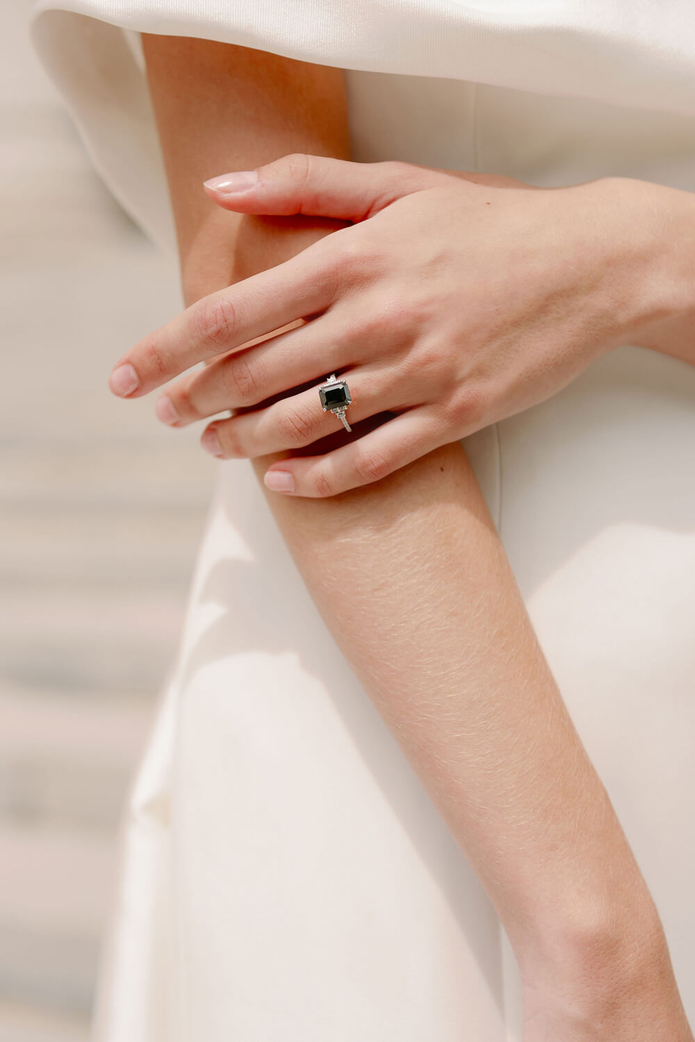Woman wearing Monique Lhuillier Fall 2023 Bliss BL23204 gown wearing a black and white diamond emerald cut ring
