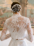 Woman wearing Monique Lhuillier Fall 2024 white Melrose lace bralette with lace long-sleeve high neck jacket and lace a-line skirt with slit