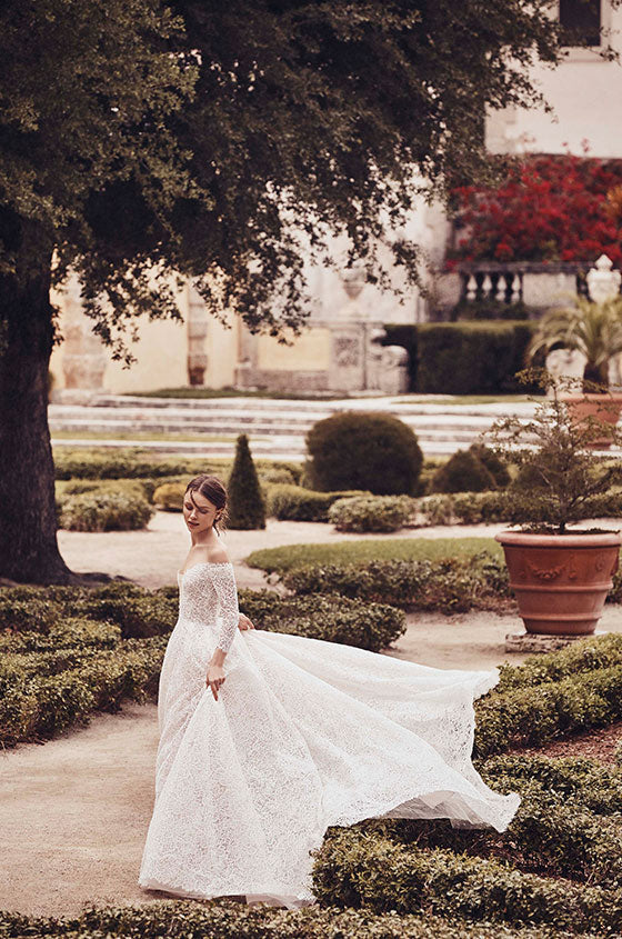Woman wearing Monique Lhuillier Spring 2020 white mosaic lace off-the-shoulder 3/4 sleeve Lovely a-line gown