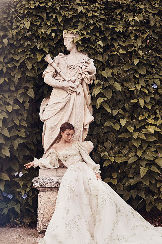 Woman wearing Monique Lhuillier Spring 2020 ivory and green floral printed off-the-shoulder Bloom a-line gown with billowed sleeve
