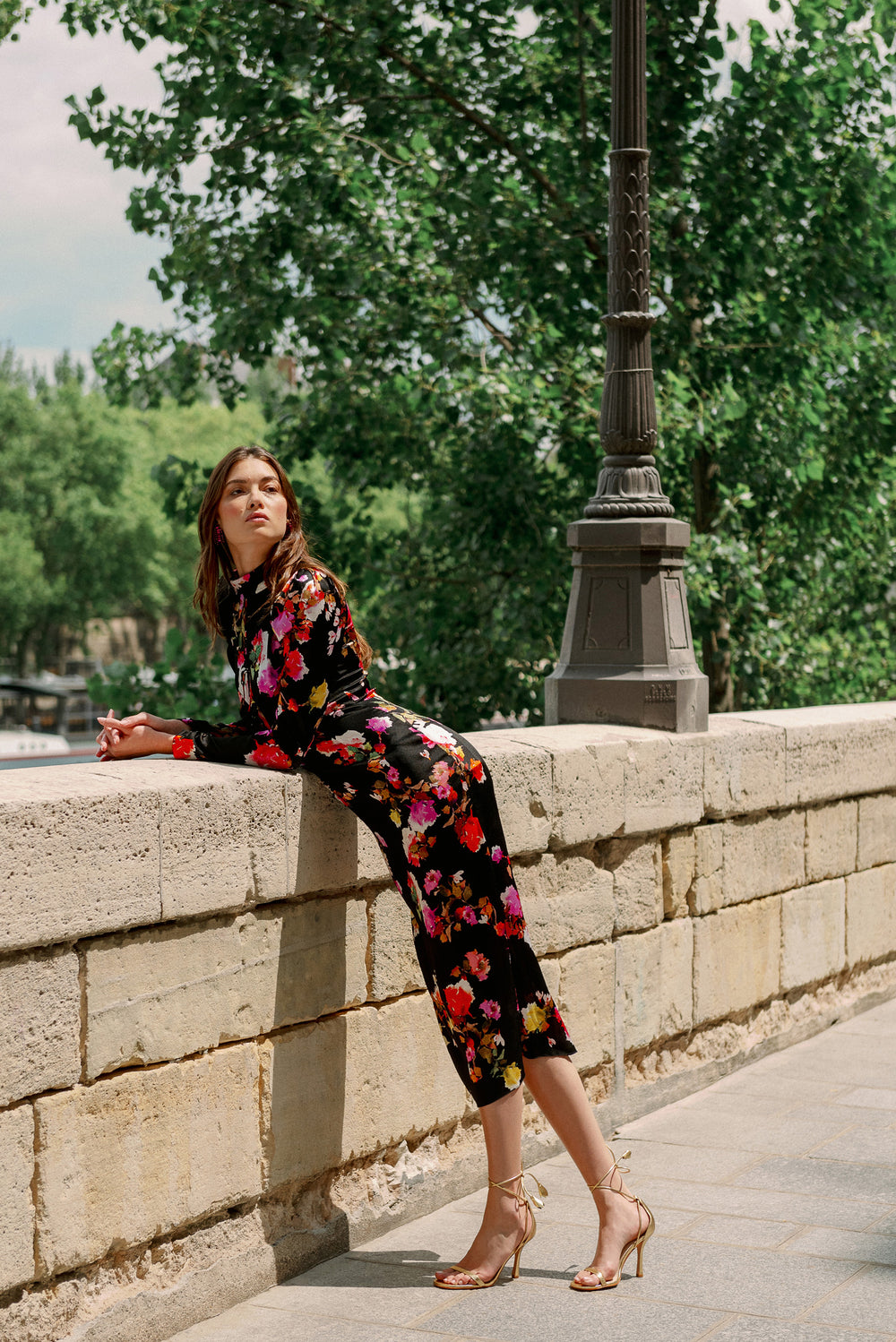 Monique Lhuillier Spring 2024 long sleeve midi dress with high neck and tied front keyhole bodice in black floral hammered silk - model leaning.