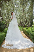 Woman in white lace Monique Lhuillier Spring 2021 Magnificent ballgown and lace long sleeve jacket and Magnificent veil with lace trim