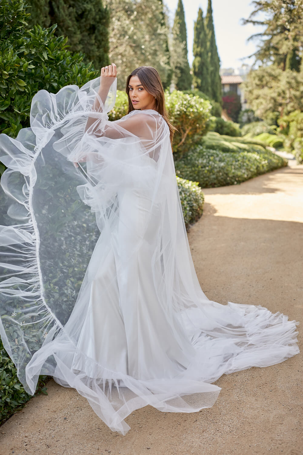 Woman wearing white tulle Monique Lhuillier Spring 2021 Roxy cape with ruffle trim