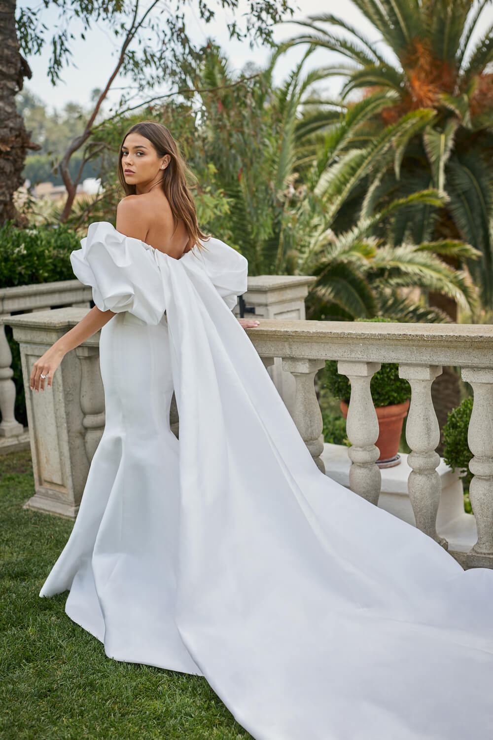 Woman wearing white Monique Lhuillier Spring 2021 mikado fitted off-the-shoulder Admire gown with Admire cape