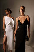 Monique Lhuillier Spring 2026 lookbook image - model on left wearing white brocade petal neckline dress with
gold ball piercing, model on right wearing noir silk wool suiting v-neck gown with pearl straps