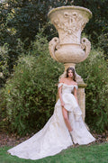 Woman wearing Monique Lhuillier Spring 2024 off-the-shoulder draped neckline high-low white and floral printed Soleil ballgown