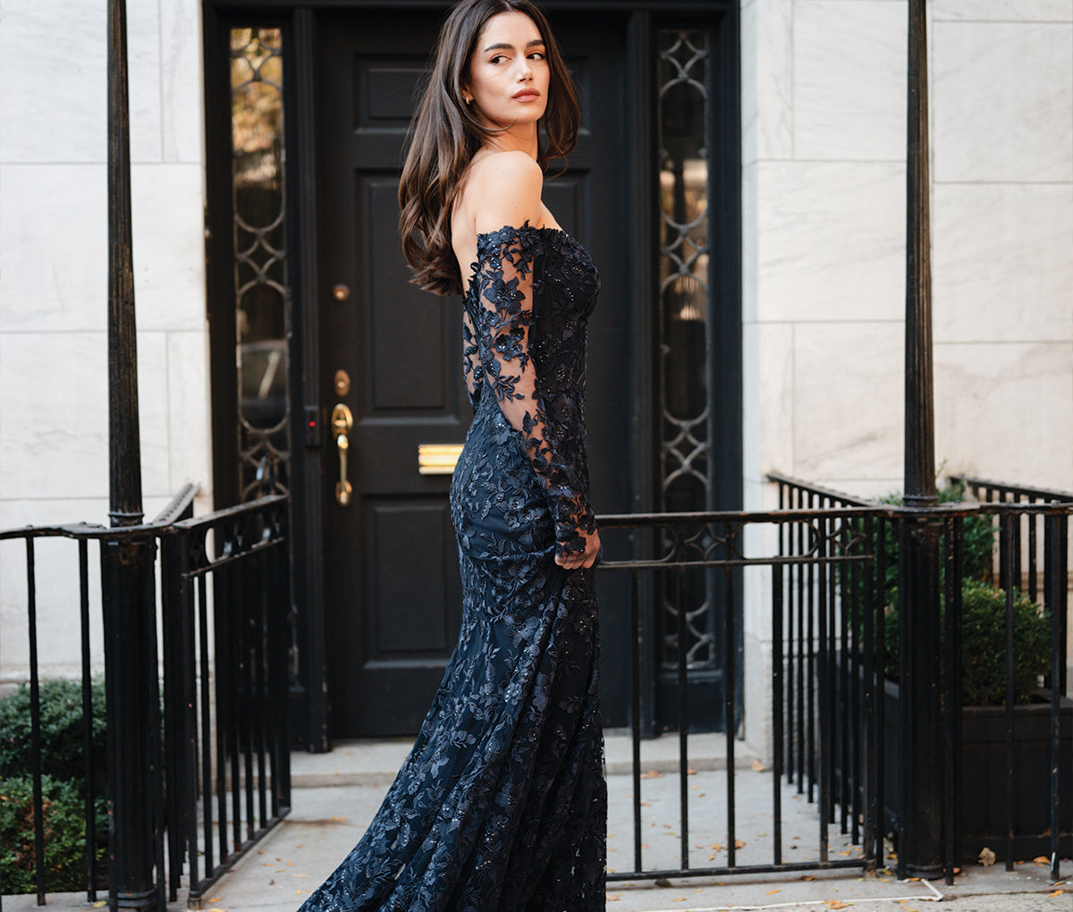 Monique Lhuillier Spring 2025 long sleeve lace navy trumpet gown on model outside in front of building