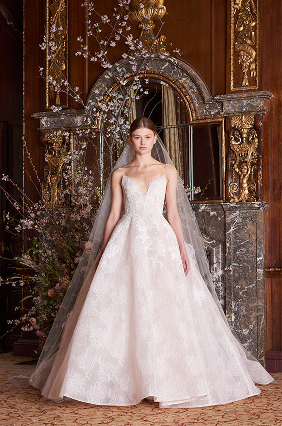Woman wearing Monique Lhuillier Spring 2019 blush strapless plunging sweetheart chantilly lace Helena ball gown with sculpted circular skirt