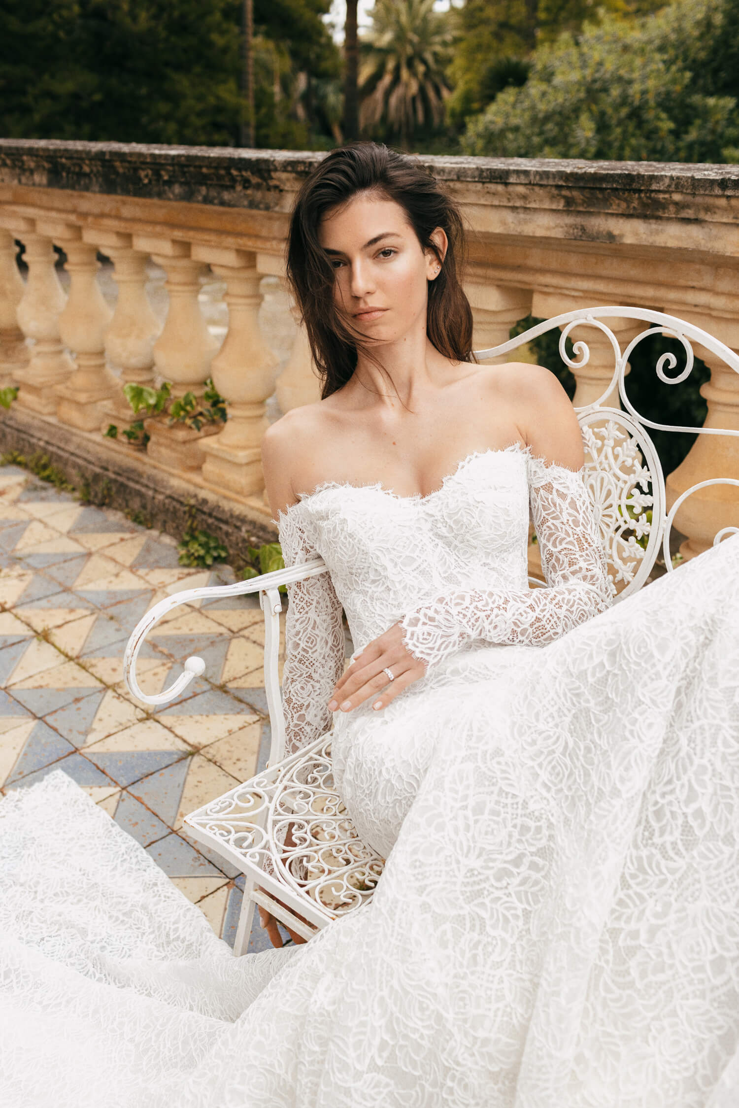 Woman wearing white long sleeve off-the-shoulder mosaic lace Monique Lhuillier Spring 2023 Viviana trumpet gown