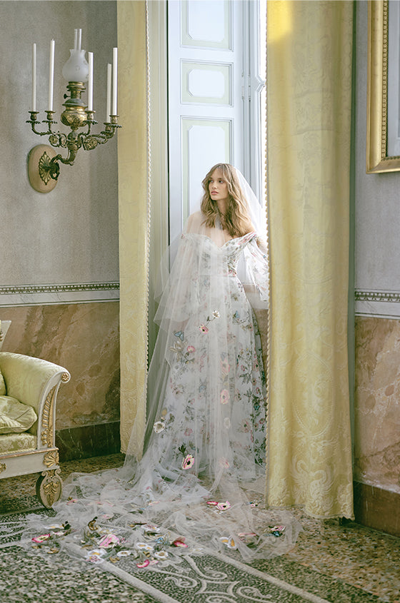 Woman wearing Monique Lhuillier Fall 2020 multi-colored floral printed off-the-shoulder organza Jardin a-line gown with billowed sleeve