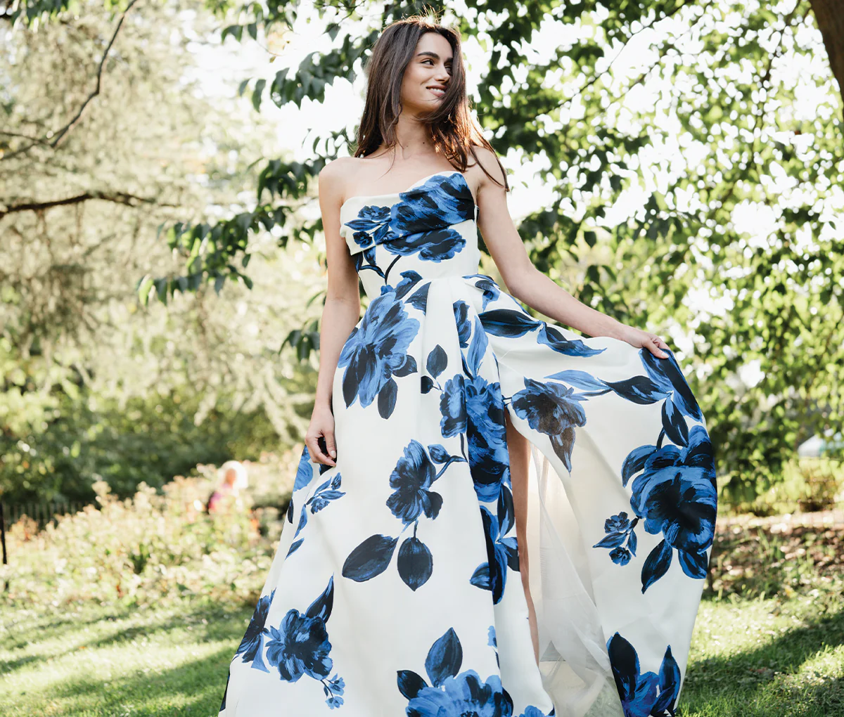 Model wearing Monique Lhuillier Spring 2025 blue and white floral printed gazar strapless ballgown with slit outside 