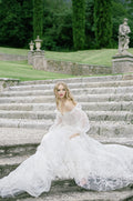 Woman wearing Monique Lhuillier Spring 2022 white embroidered a-line Splendid gown with off-the-shoulder billowed sleeve
