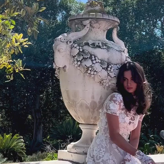 Women leaning on railing in Monique Lhuillier Bridal Spring 2024 blush and white floral embroidered Antoinette gown, jacket and gloves. 