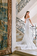 Woman wearing Monique Lhuillier Fall 2023 white off-the-shoulder fitted lace Desire trumpet gown with long train